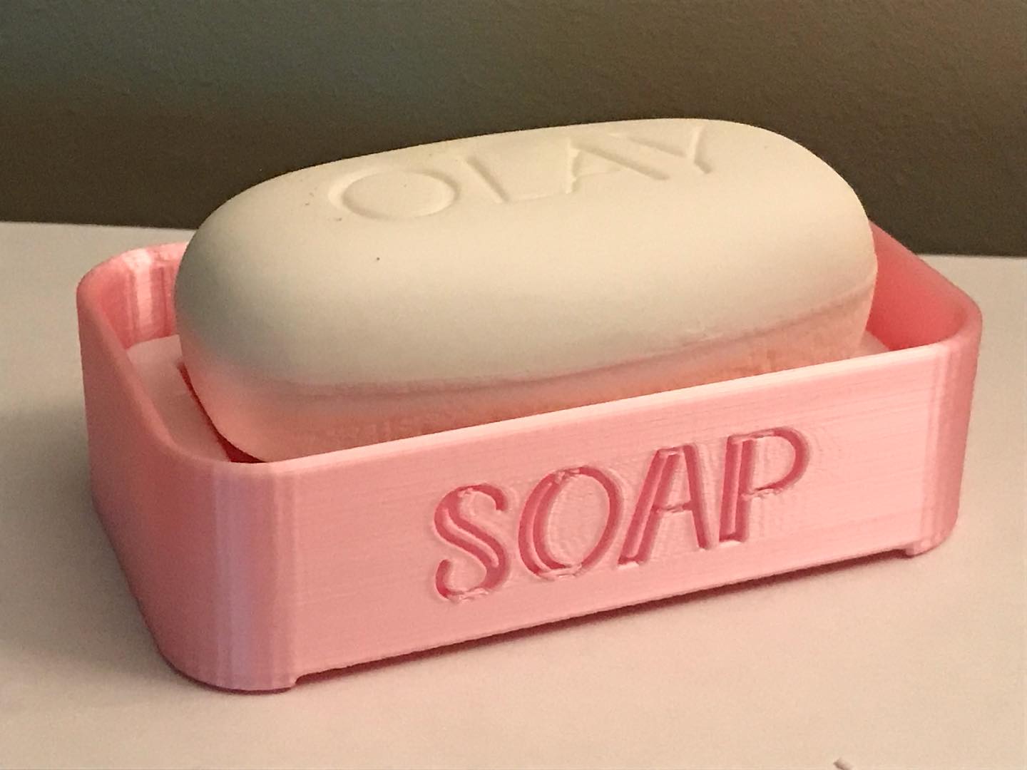 Pink Soap holder with the word Soap embossed into it, it is holding a bar of soap.